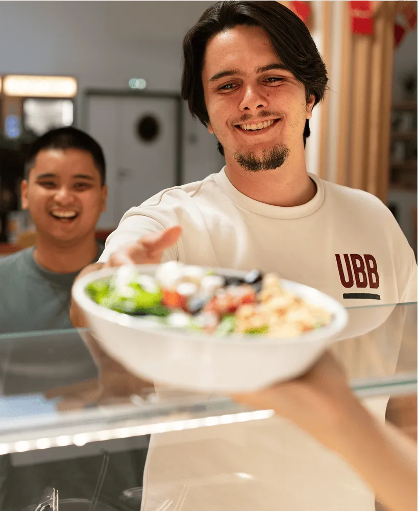 une jeune homme montre une salade composée qu'il a pris à la cantine de son lieu de travail