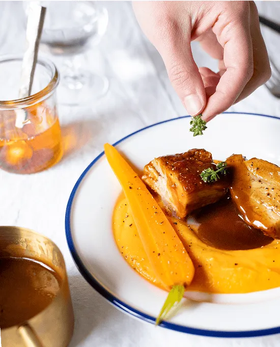 une personne ajoute une herbe sur un plat composé d'une purée de carottes et de viande blanche préparé par Popchef