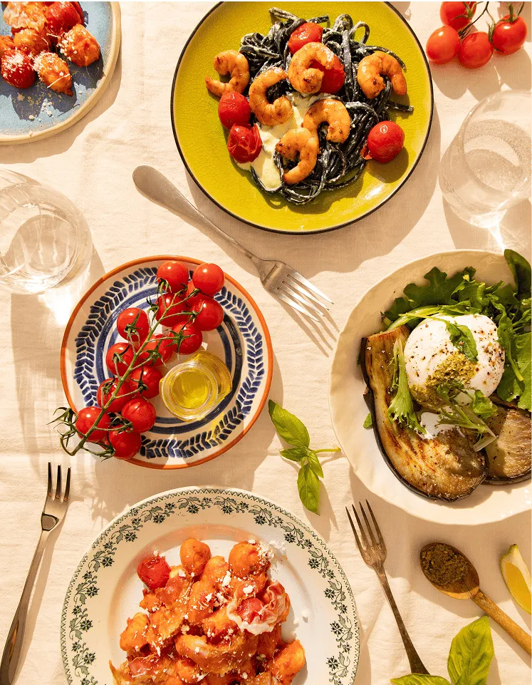 Table dressée avec différents plats cuisinés par Popchef : gnocchis à la tomate, pâtes aux crevettes, burrata avec légumes grillés et tomates cerises