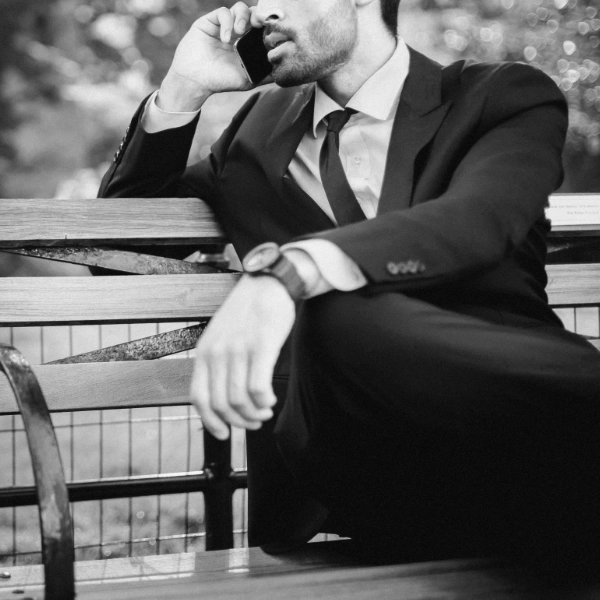 Black and white photo of a person in a suit sitting on a bench, having a therapy session on a mobile phone.