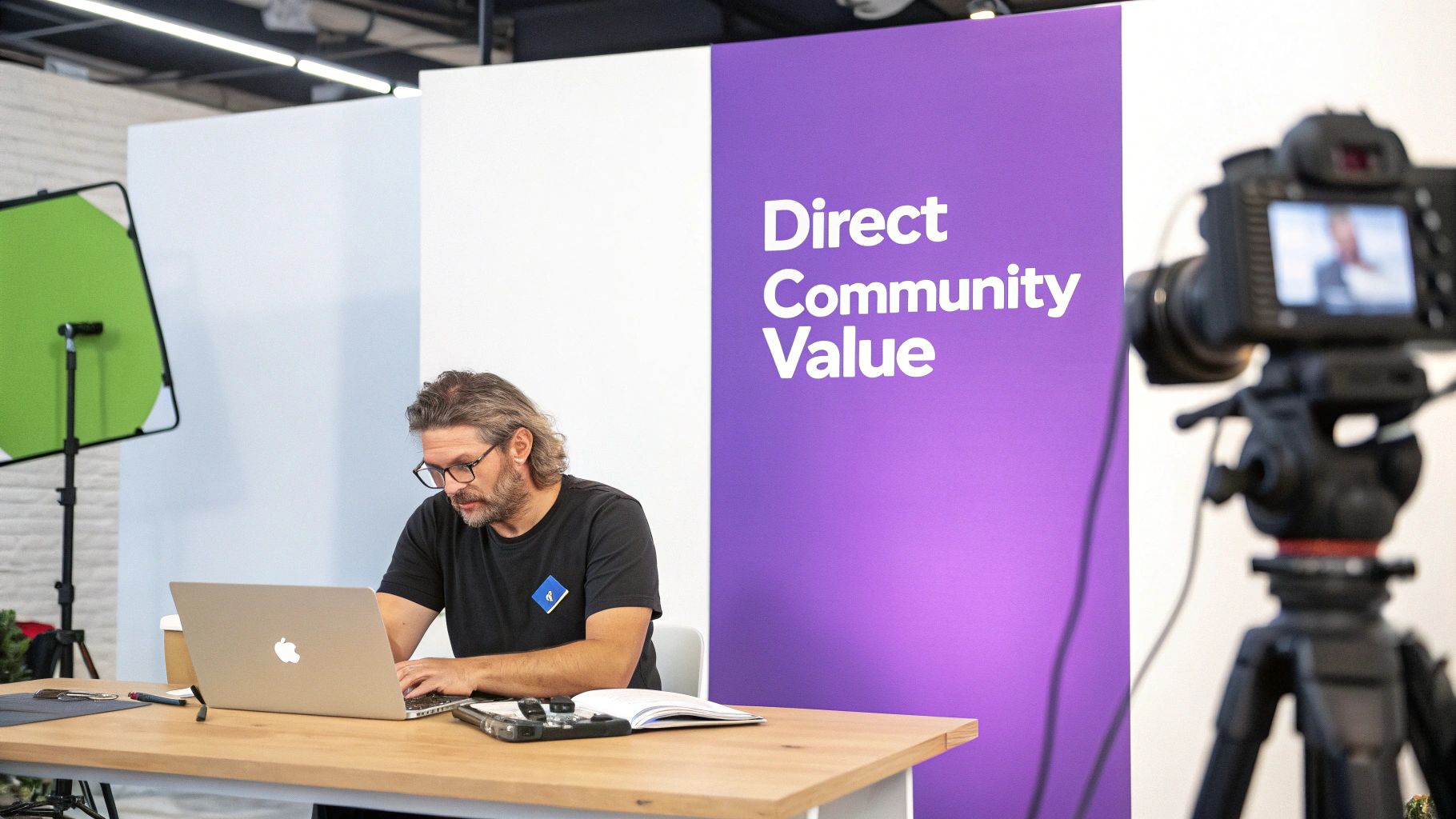 A man with glasses and a beard works on a laptop during a recording session with a 'Direct Community Value' backdrop.
