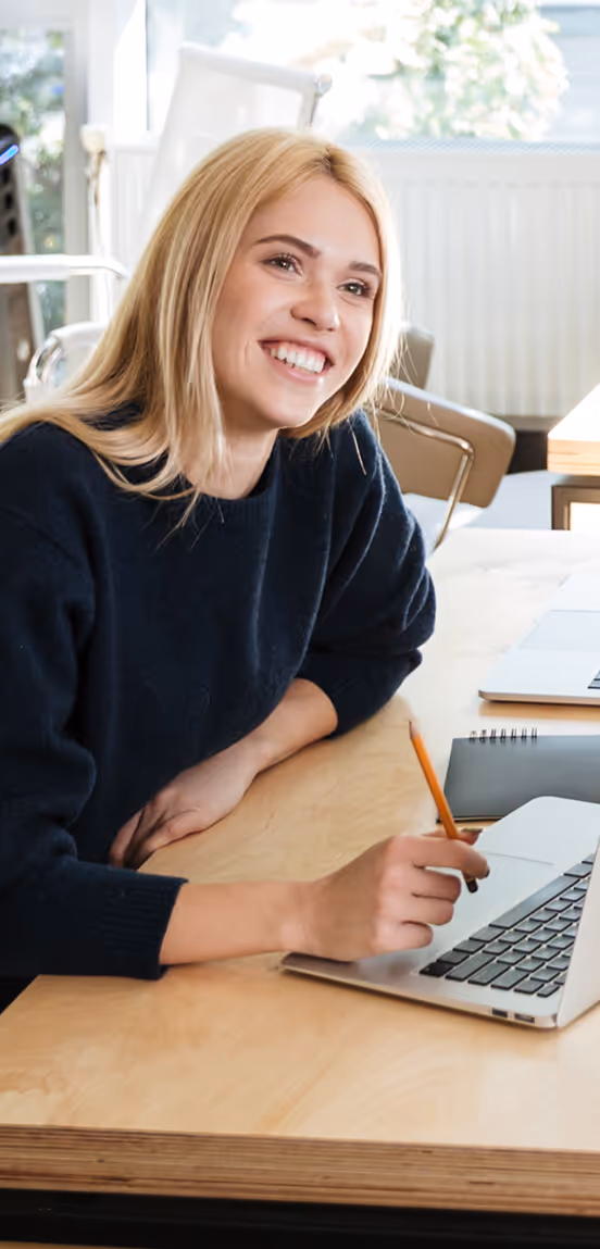 Femme souriante travaillant sur un ordinateur portable à un bureau moderne et lumineux.