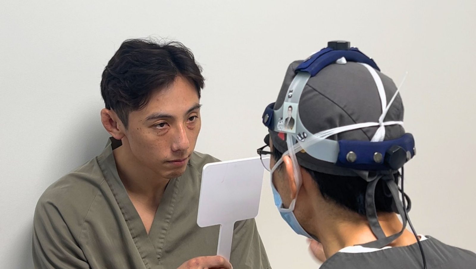 A doctor with a headlamp holding a mirror for a patient during a consultation