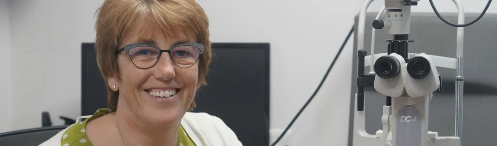 Smiling optometrist with eye examination equipment in clinical setting