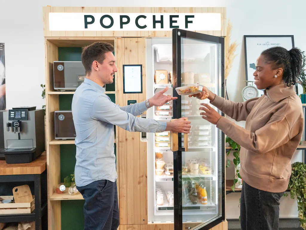 Deux jeunes hommes qui se servent à manger dans un frigo connecté Popchef