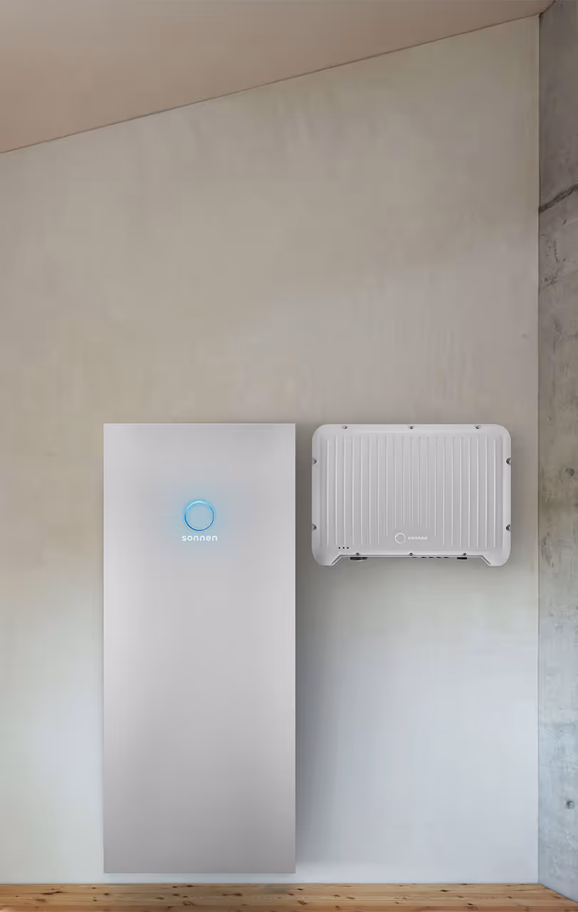 Zwei Geräte zur Wandmontage im Innenraum: links eine moderne weiße sonnenBatterie mit leuchtendem Ring, rechts ein rechteckiger sonnen Wechselrichter mit geripptem Gehäuse.