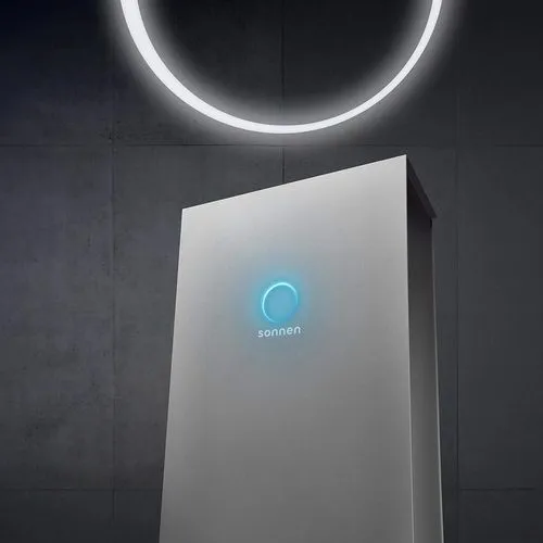 sonnenBatterie med lysande blå logga i ett rum med mörk vägg och lysande ljusring.