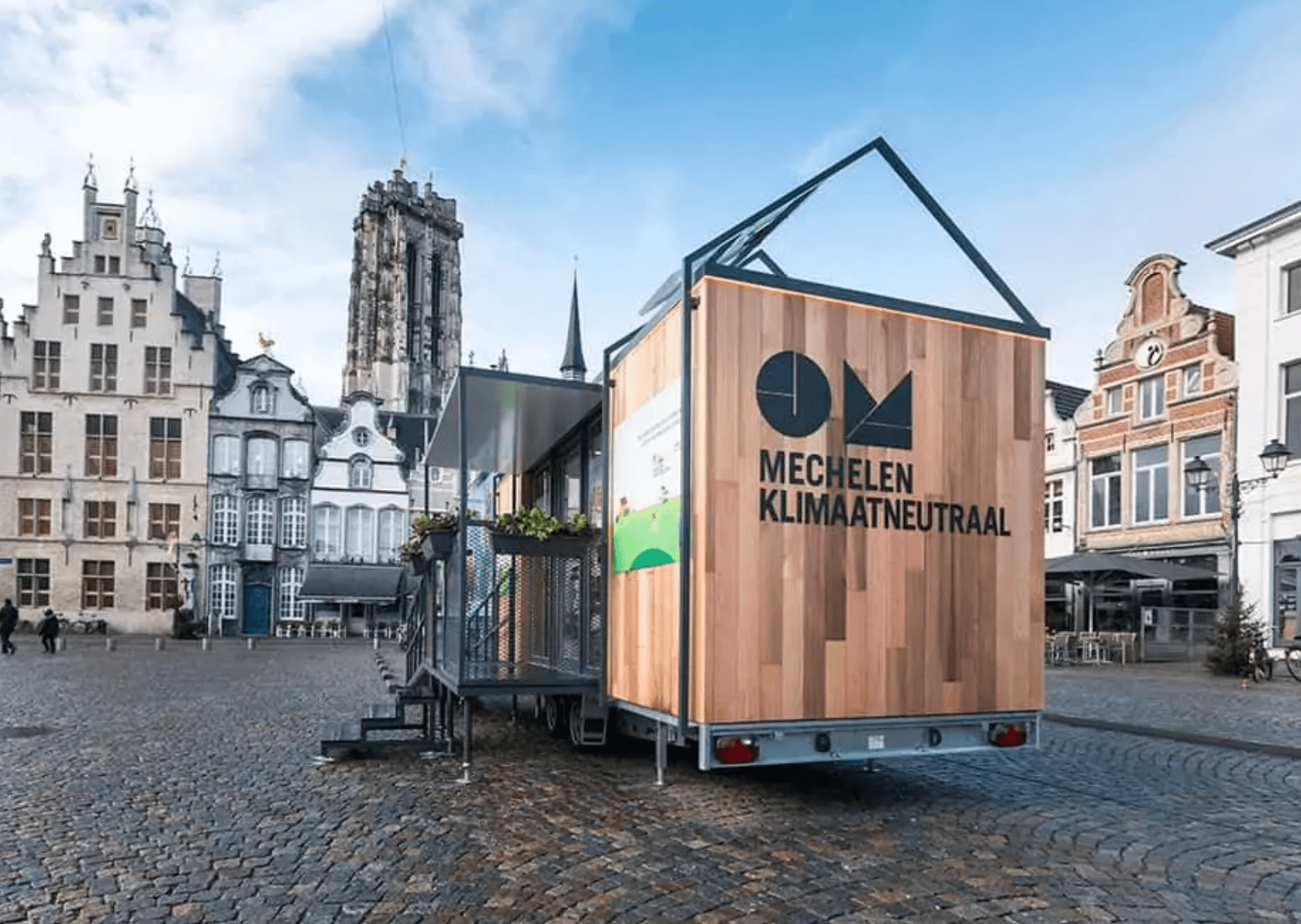 Wood-paneled mobile structure with Mechelen Klimaatneutraal text in historical European town square.
