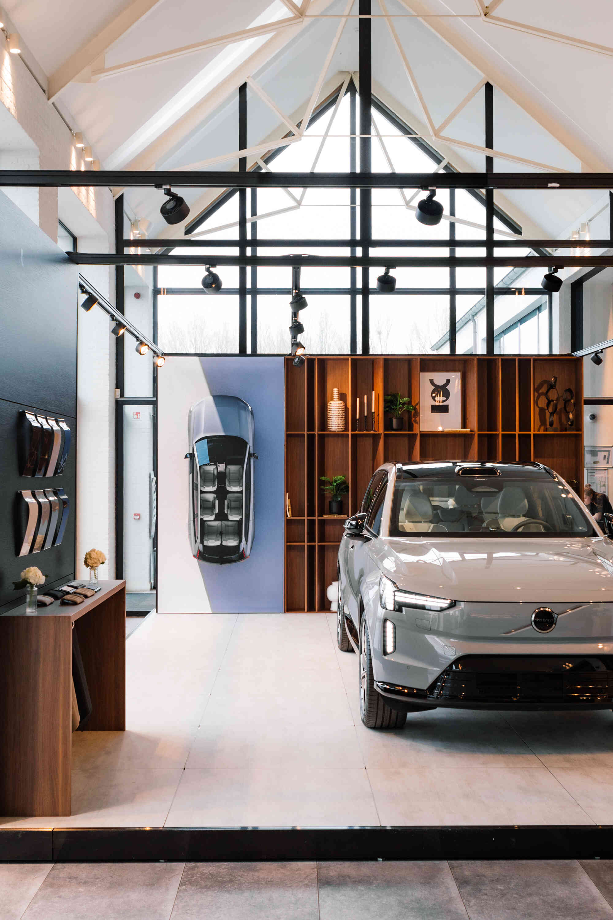 Modern white Volvo SUV displayed in a bright showroom with wooden shelves and decor behind it.