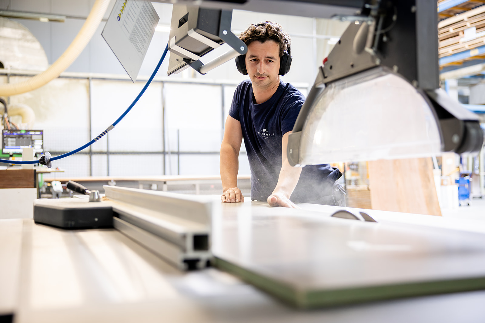 Man wearing headphones operates a large industrial table saw in a bright workshop.