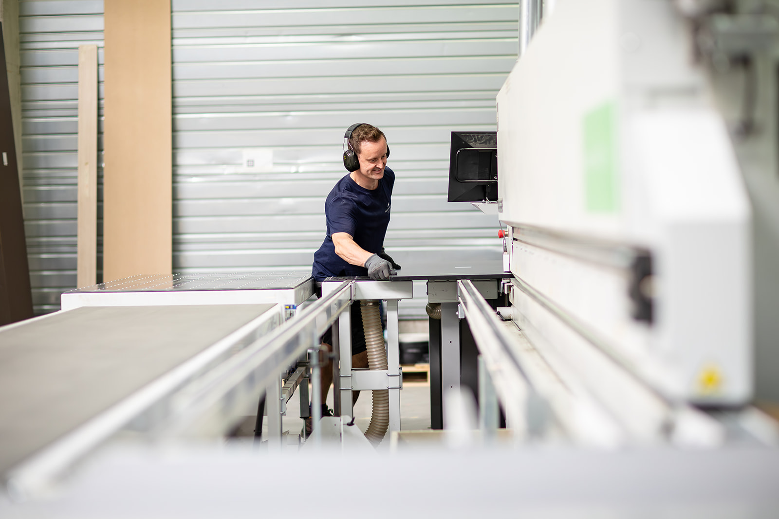 Man wearing gloves and ear protectors operating a large cutting machine in a workshop.