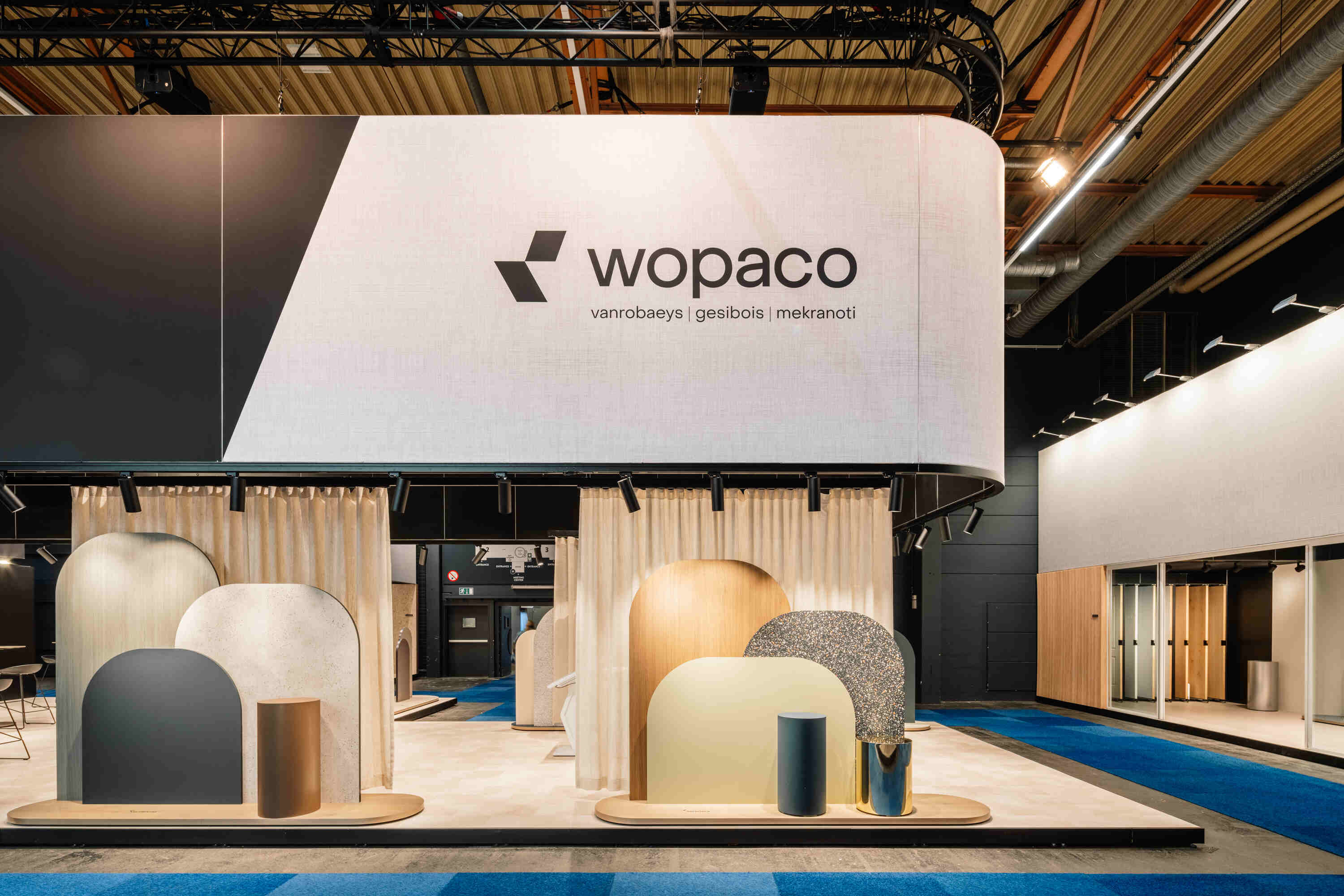 Stand d'exposition Wopaco avec des panneaux décoratifs modernes et des présentoirs cylindriques dans la salle d'exposition.