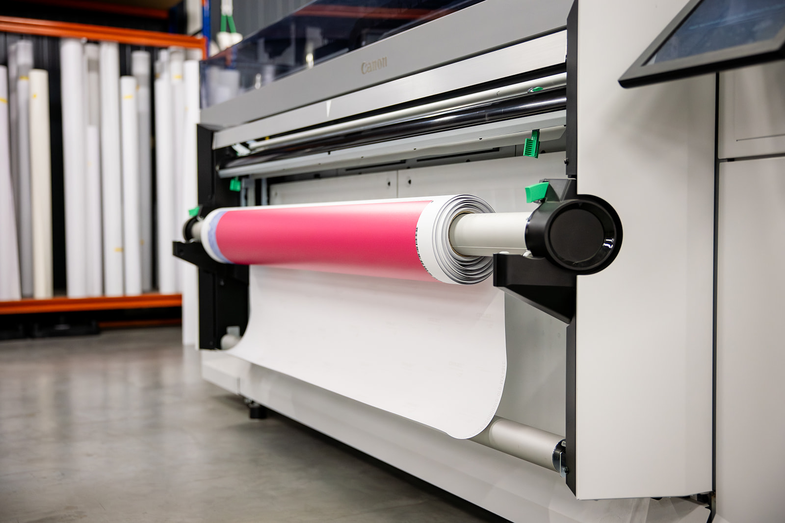 Large Canon printer printing on a roll of white paper with a pink section in a printing shop.