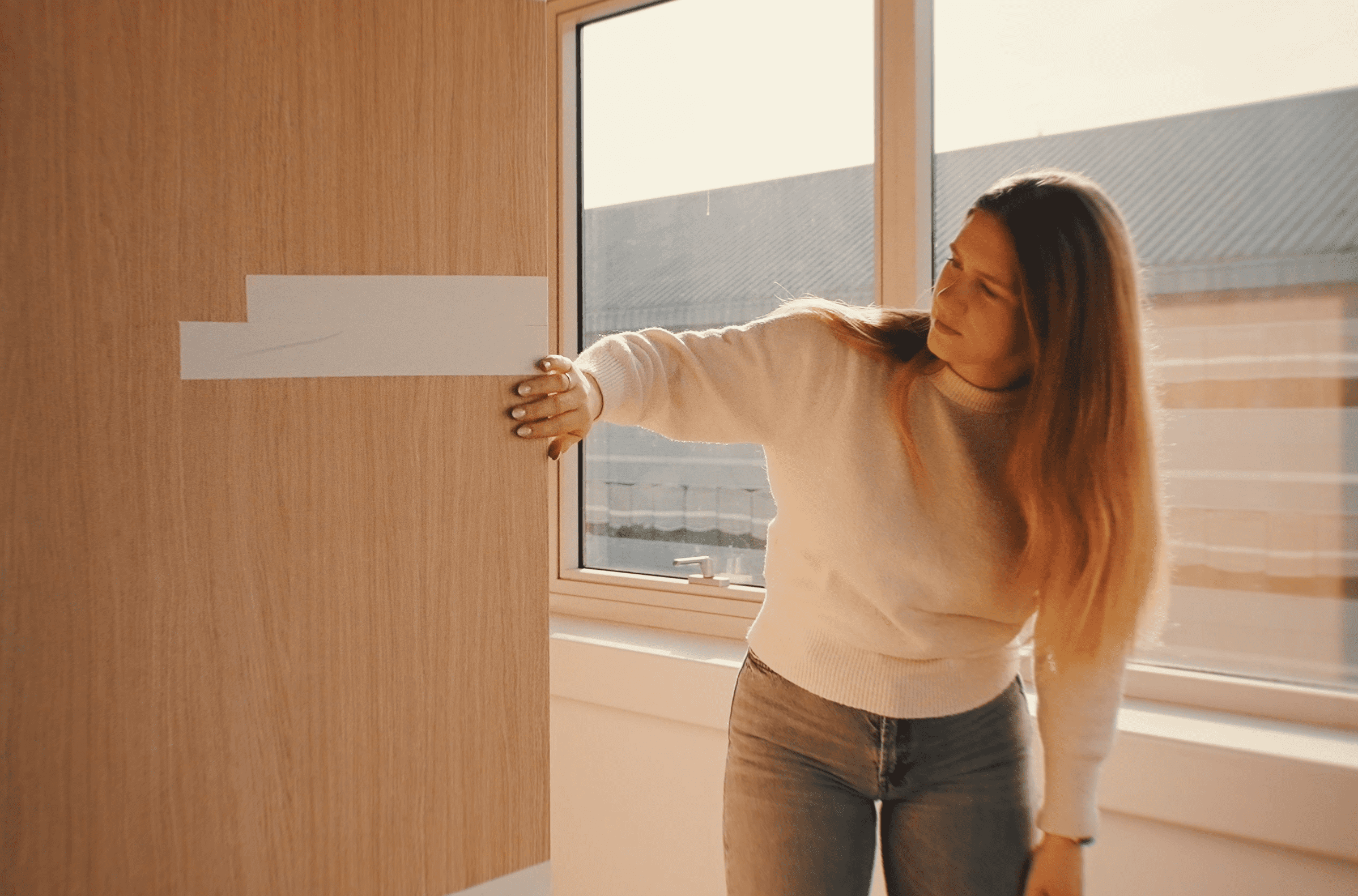 Femme en pull et jean ouvrant une porte en bois avec fenêtre.