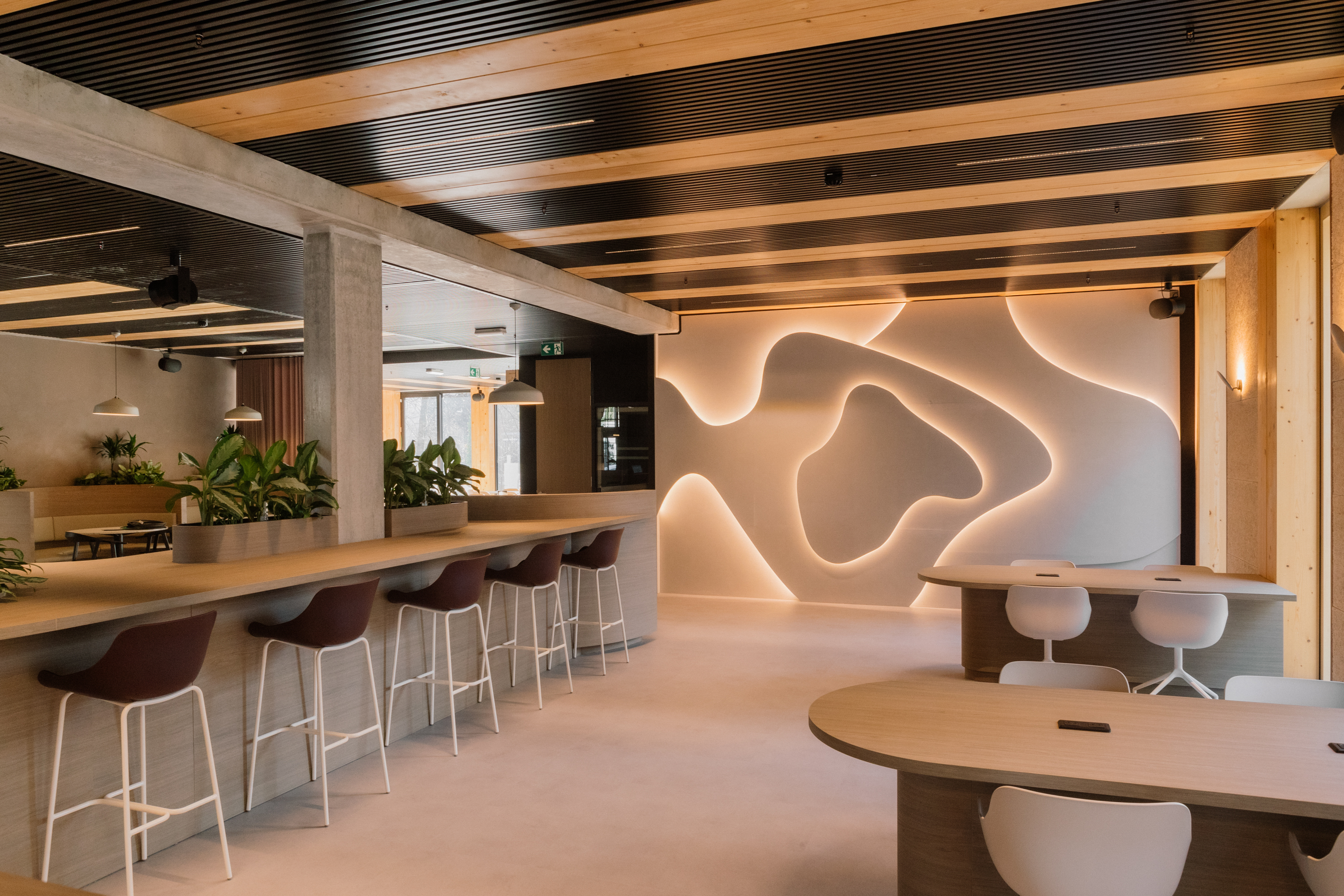 Modern kantoorruimte met hoge barkrukken, planten en golvende LED-wandverlichting.