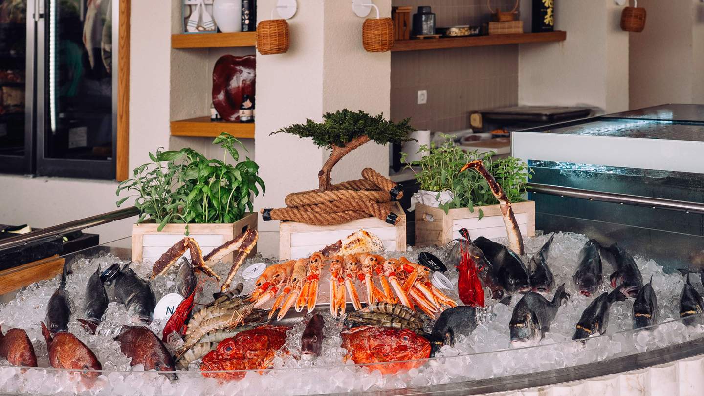 A seafood display featuring various fish and shellfish on a bed of ice, with greenery in wooden crates and decorative elements in a modern setting.