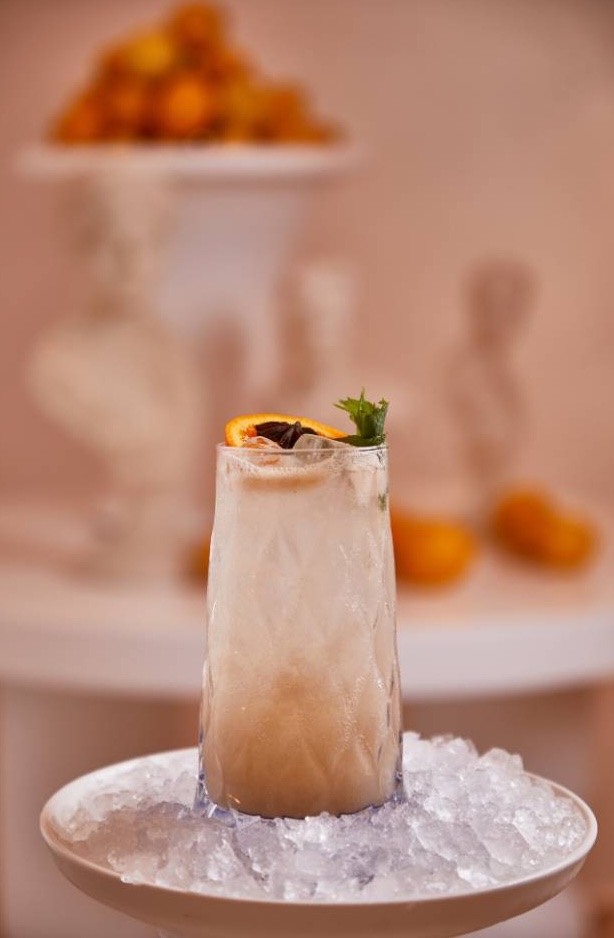 Iced cocktail with orange slice and mint garnish on crushed ice, blurred fruits background