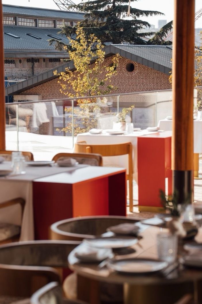 Modern restaurant interior with red accents overlooking brick buildings and autumn foliage