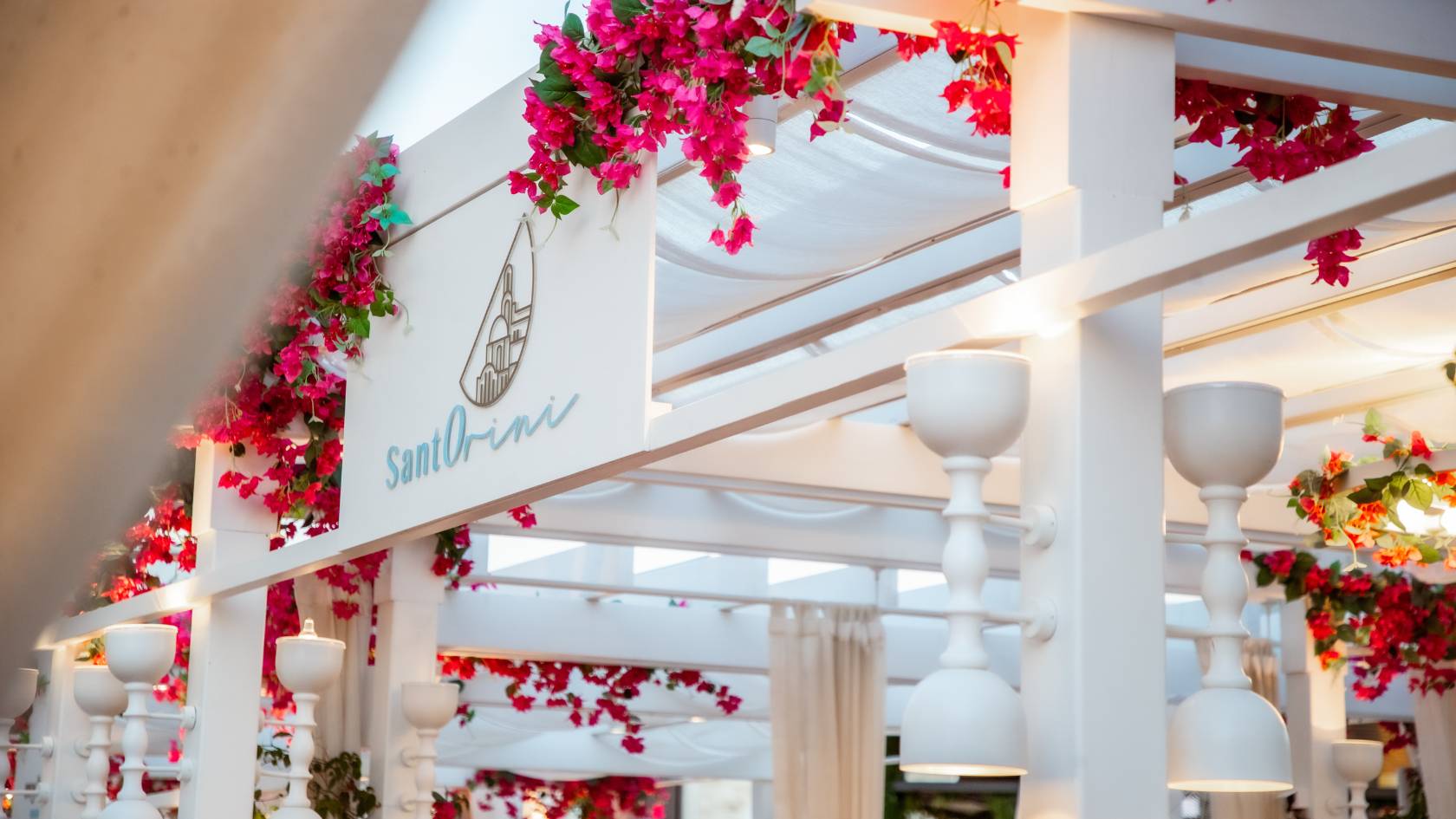 Elegant white pergola decorated with vibrant pink and red hanging flowers and signage