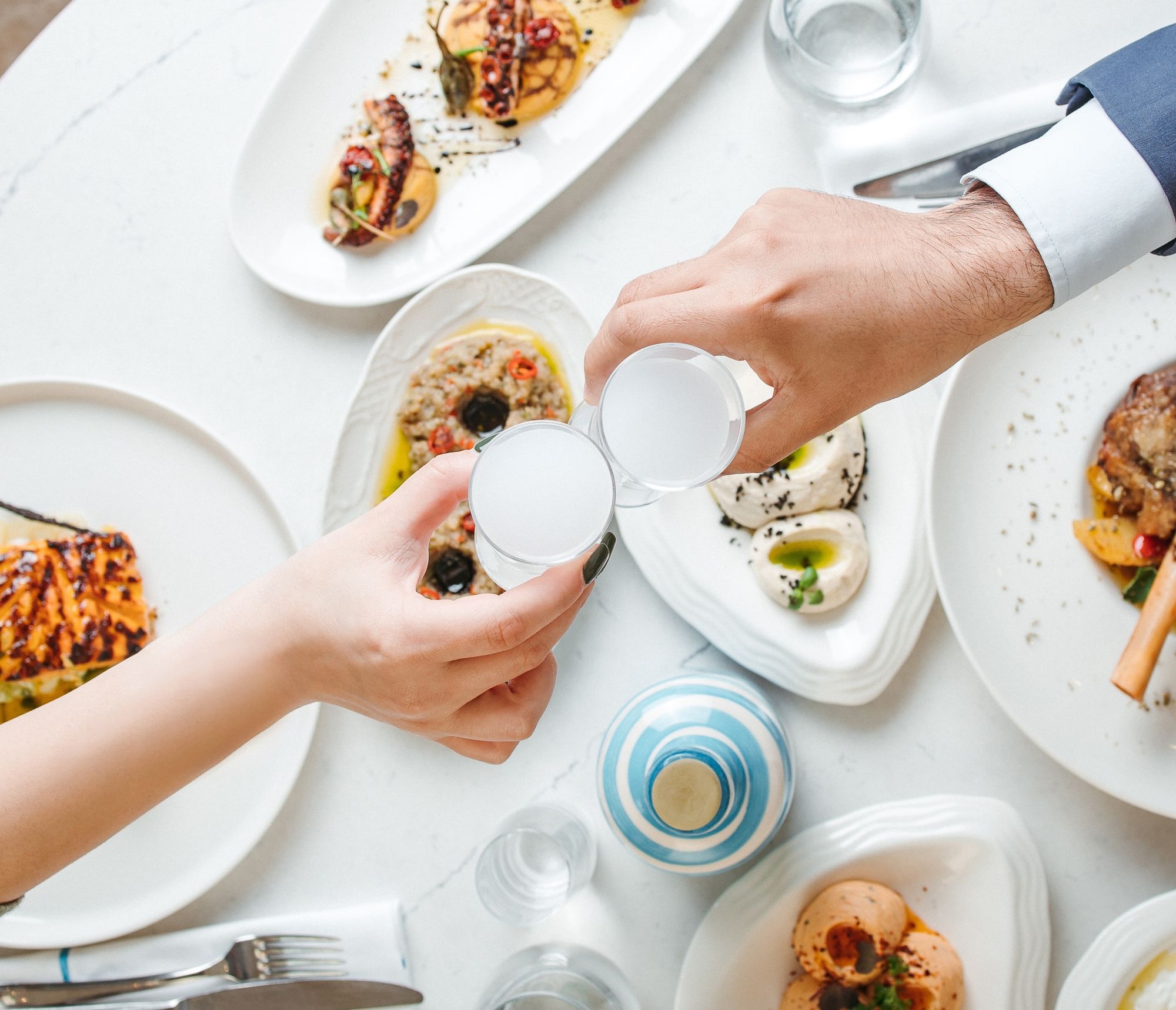 Two people clinking water glasses over plated gourmet seafood and appetizers at fine dining table