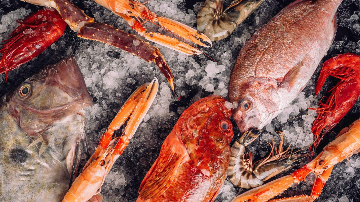 Fresh seafood including fish, prawns, and lobsters displayed on crushed ice at market.