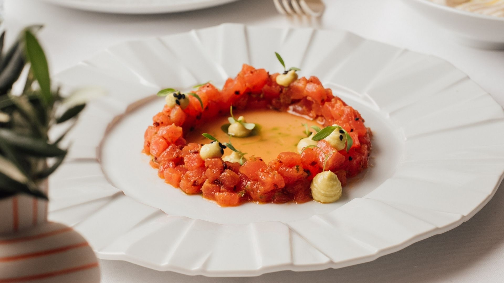 Fine dining plate with diced red tuna, orange sauce, and herb garnish on white plate
