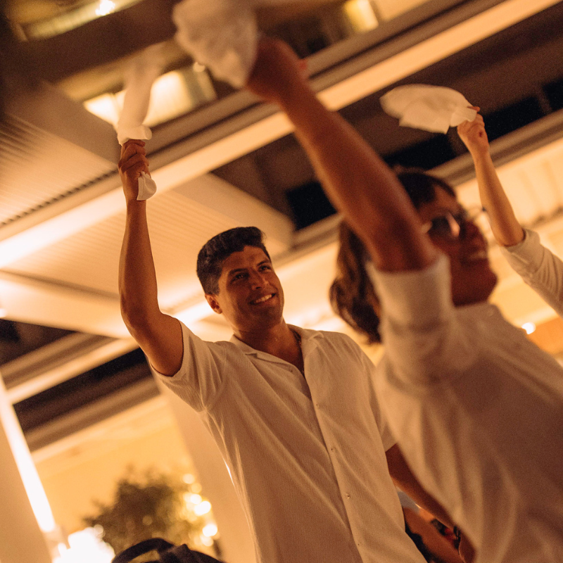 Man in white shirt holding white paper, celebrating with others indoors.