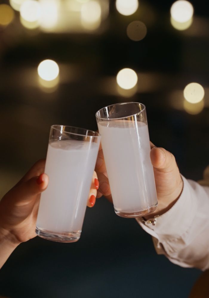 Two hands toasting with glasses of clear liquid against blurred bokeh lights
