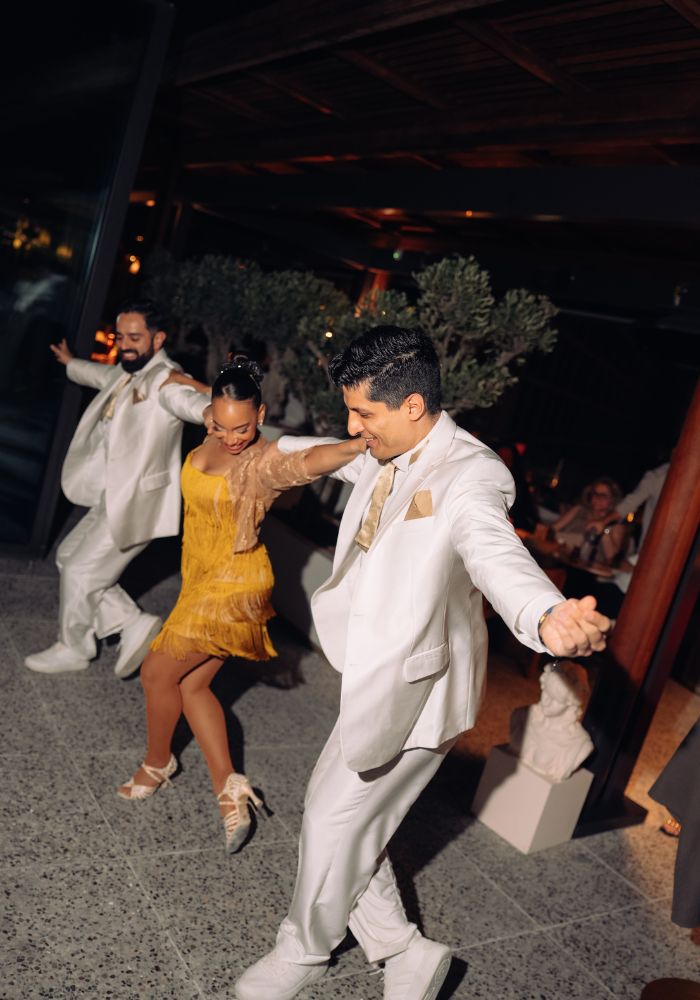 Well-dressed men and woman dancing joyfully at a festive outdoor evening celebration event.