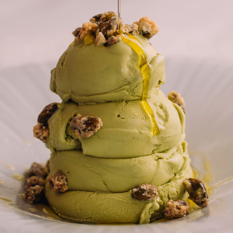 Stack of pistachio ice cream scoops topped with cookie crumbles and caramel drizzle