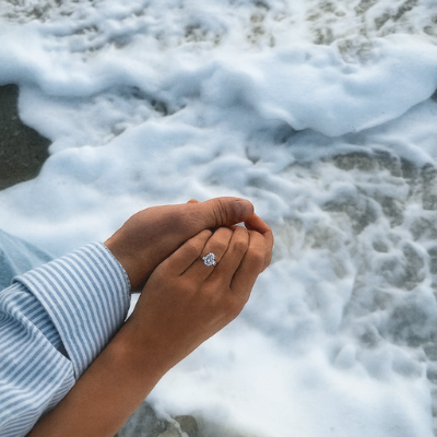Hand displaying diamond ring over ocean waves and rocky shore