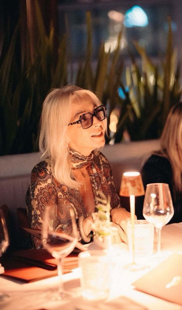 Woman wearing glasses at elegant evening dinner with glowing glasses and ambient lighting.