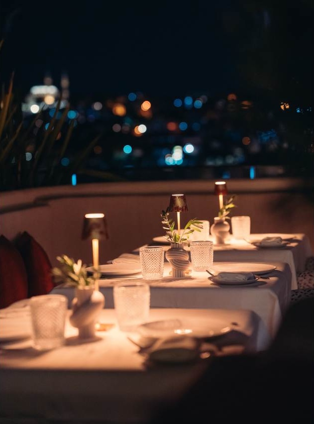 Elegant outdoor dinner table set at night with city lights bokeh background and candles
