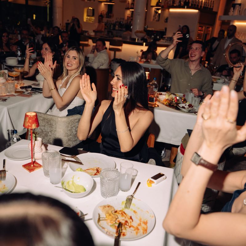 People enjoying dinner and clapping at an elegant indoor event or party celebration.
