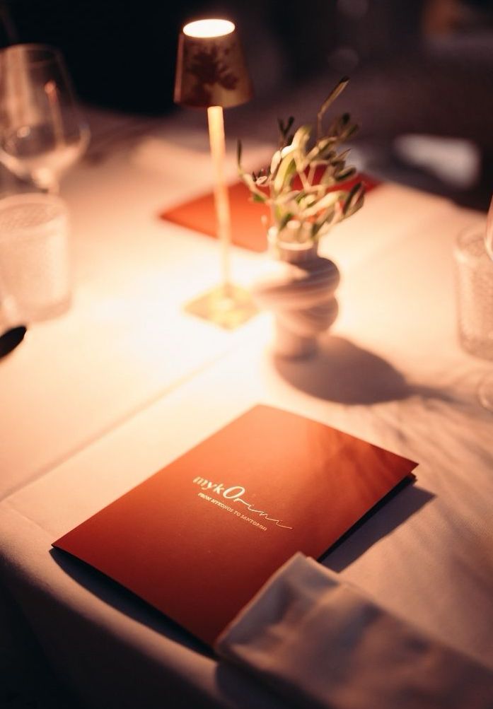 Elegant table setting with red menu card, flowers, lamp, and glasses at fine dining restaurant.