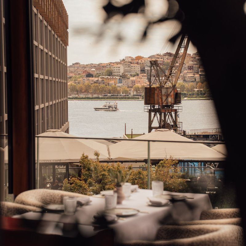 View of riverside city and docked cargo crane from a restaurant window with table setting