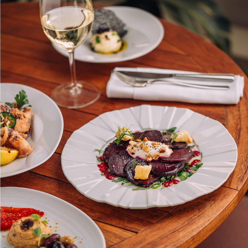 Fine dining table with white wine, beet salad, and gourmet plates on wooden table.