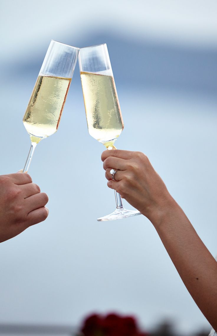 Two hands clinking champagne flutes filled with sparkling wine against blue sky