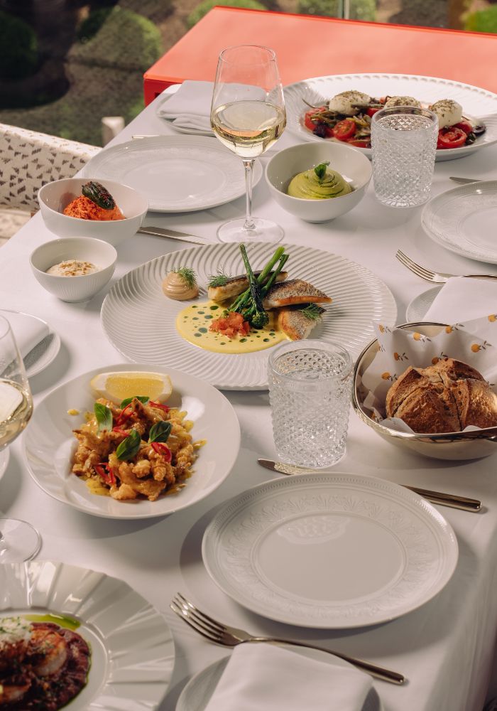 Elegant fine dining table with white plates, wine glass, gourmet dishes, and place settings.