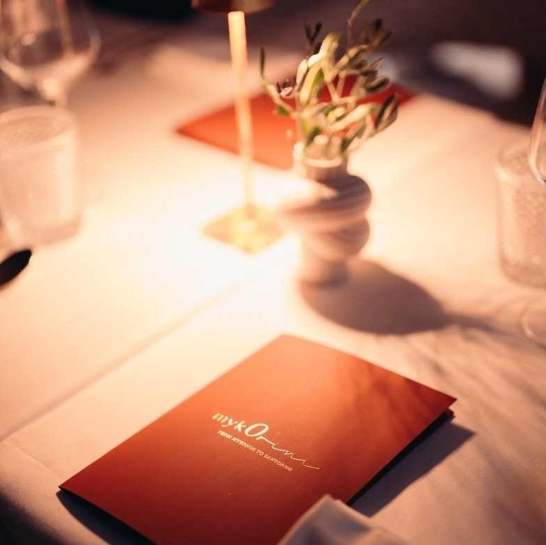 Red menu card on white dining table with floral centerpiece and candles.