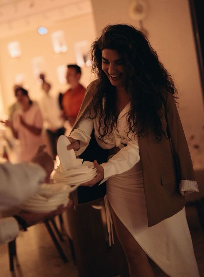 Smiling woman dancing at a warm-lit indoor party with blurred guests in background