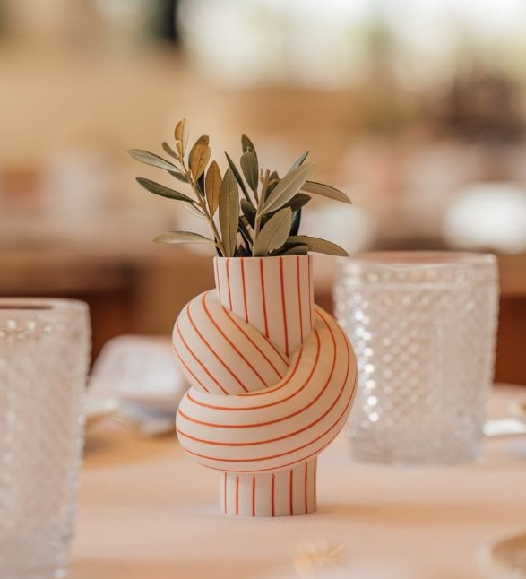 Modern ceramic vase with red striped pattern holding dried olive branches