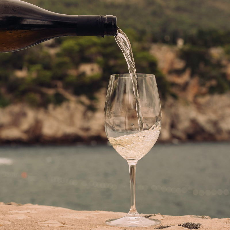White wine being poured into a glass overlooking a scenic riverside landscape