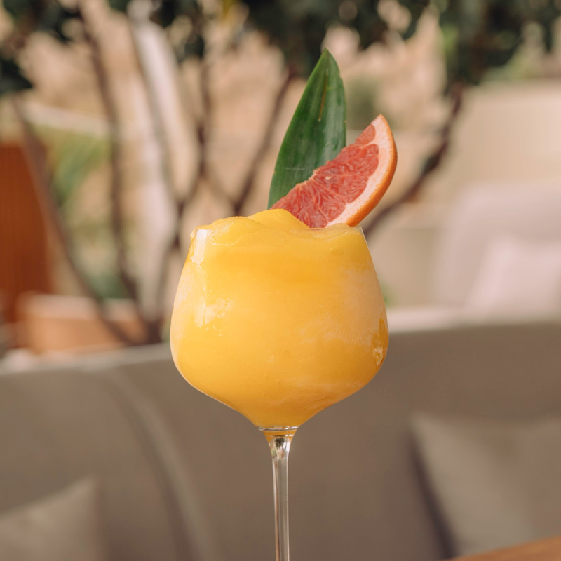 Bright yellow cocktail with grapefruit slice and mint leaf garnish outdoors