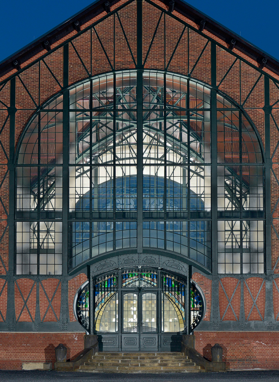 Front view of the historic entrance hall of Zeche Zollern in Dortmund, featuring a large arched steel-and-glass façade with decorative stained-glass details and red brick architecture.