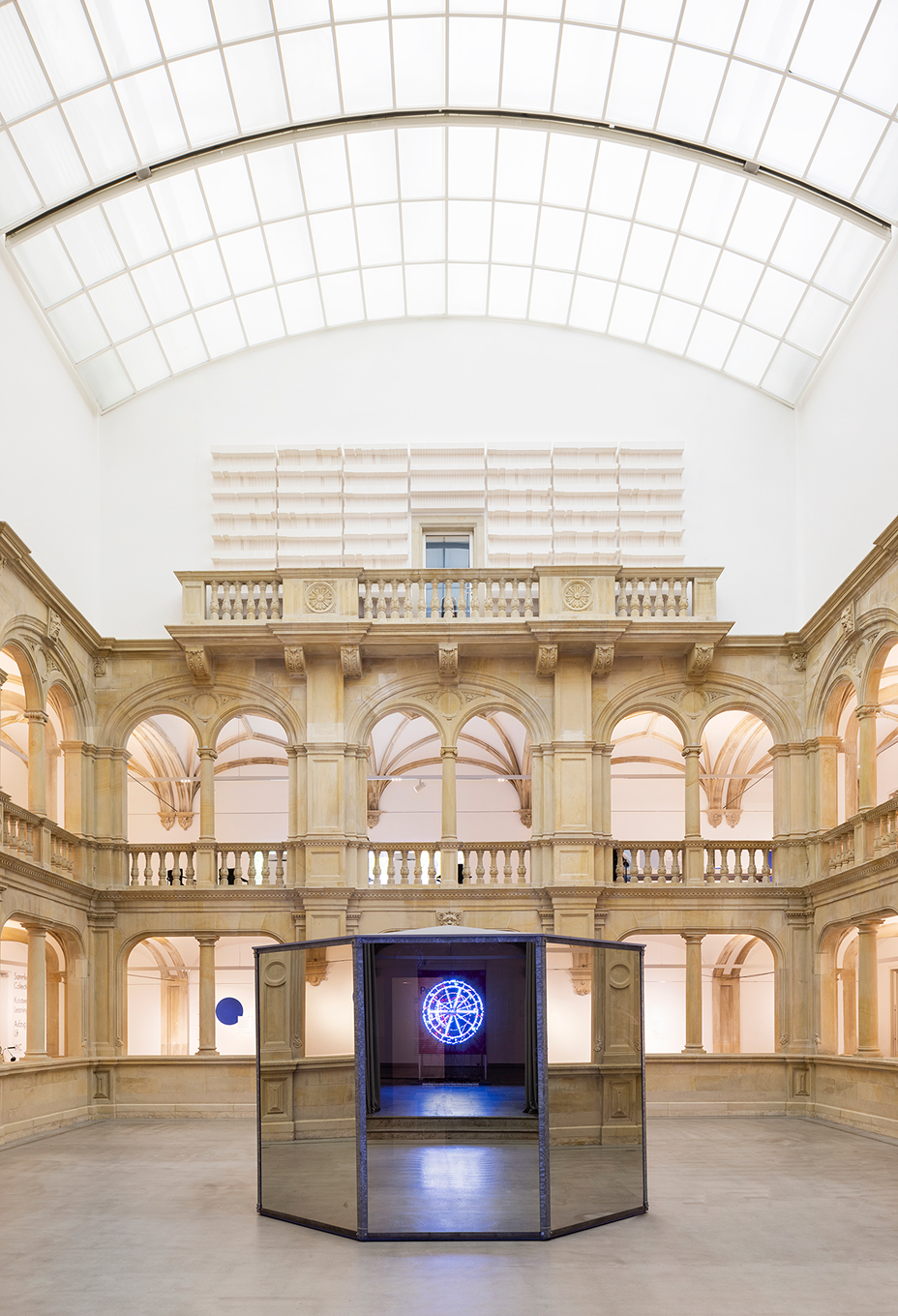Interior view of the Museum für Kunst und Kultur in Münster, showing the central atrium with historic arches, a modern glass roof, and a contemporary art installation in the center.