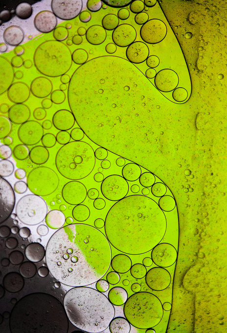 Macro shot of oil and water patterns in vibrant green and black, forming organic shapes.