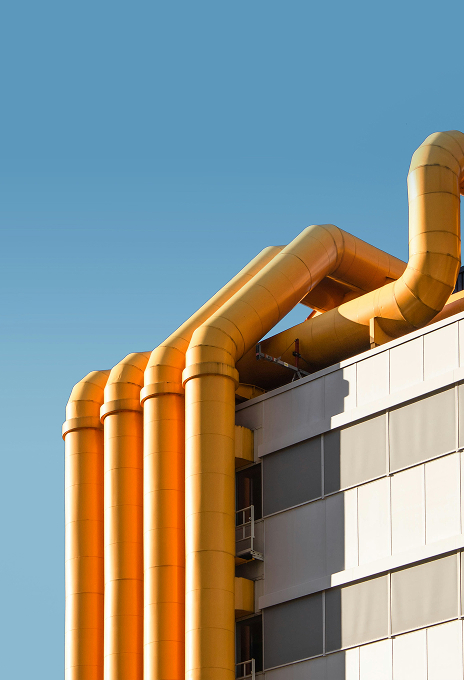 Yellow industrial pipes on the exterior of a modern building against a clear blue sky, symbolizing process flow and innovation.
