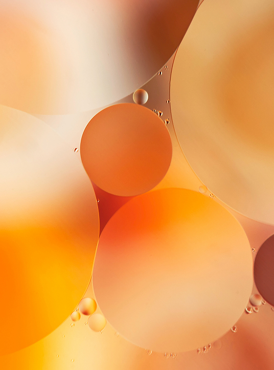 Close-up of orange-toned oil droplets in liquid, representing transformation and the plant-based raw materials used by Simplyfined.