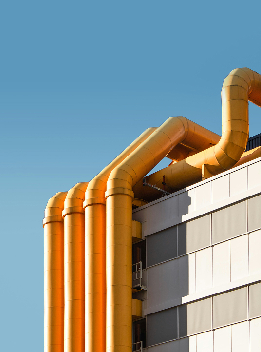 Yellow industrial pipes on the exterior of a modern building against a clear blue sky, symbolizing process flow and innovation.